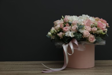 Gift box with bouquet of beautiful flowers and eucalyptus branches on wooden table against black background. Space for text