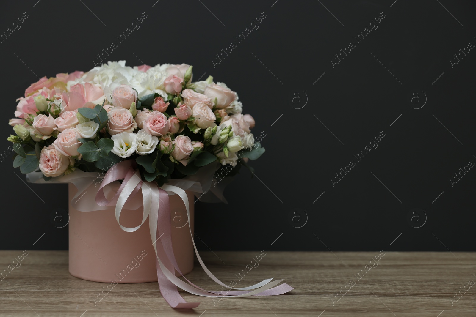 Photo of Gift box with bouquet of beautiful flowers and eucalyptus branches on wooden table against black background. Space for text