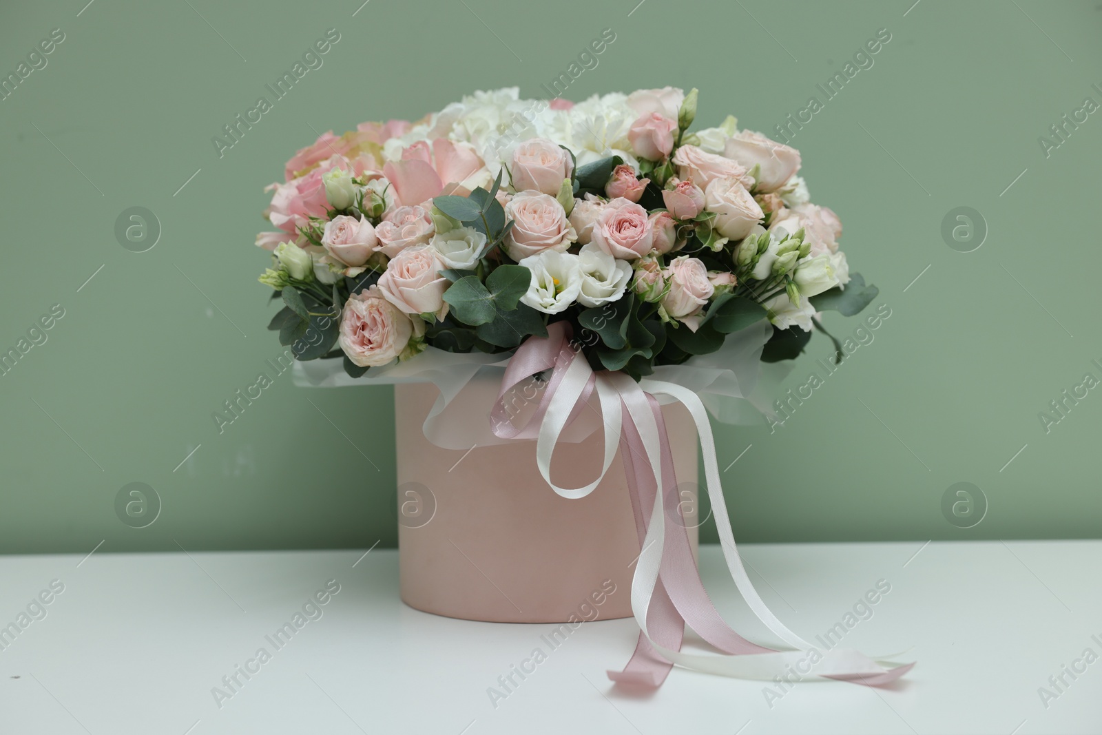 Photo of Gift box with bouquet of beautiful flowers and eucalyptus branches on white table against green background