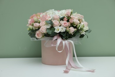 Gift box with bouquet of beautiful flowers and eucalyptus branches on white table against green background