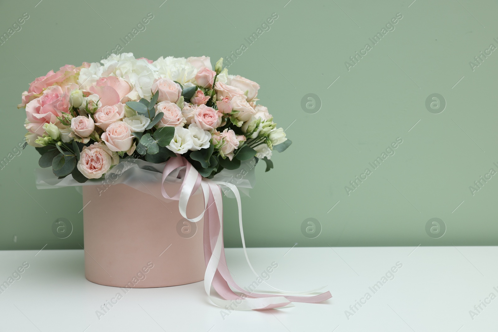 Photo of Gift box with bouquet of beautiful flowers and eucalyptus branches on white table against green background. Space for text