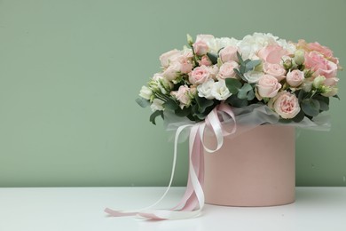 Gift box with bouquet of beautiful flowers and eucalyptus branches on white table against green background. Space for text