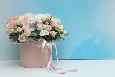 Photo of Gift box with bouquet of beautiful flowers and eucalyptus branches on white table against light blue background. Space for text