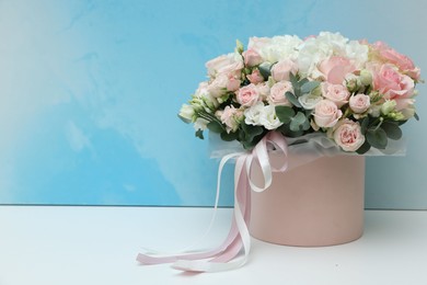 Gift box with bouquet of beautiful flowers and eucalyptus branches on white table against light blue background. Space for text