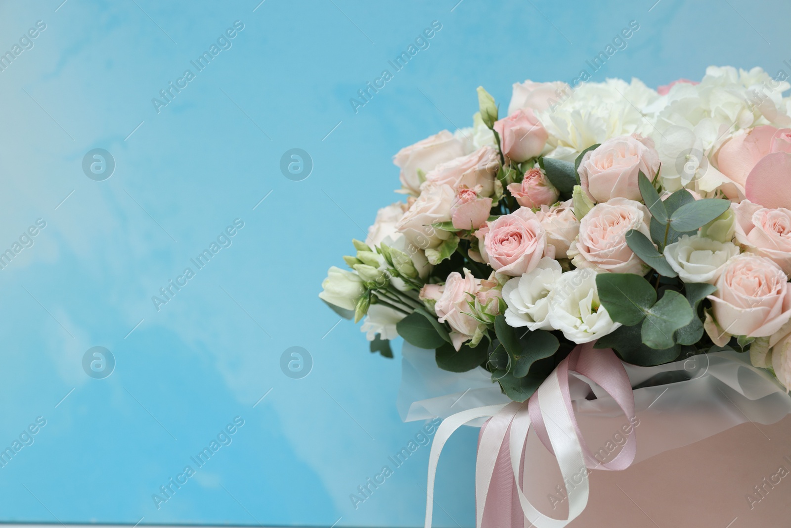 Photo of Bouquet of beautiful flowers and eucalyptus branches on light blue background, closeup. Space for text