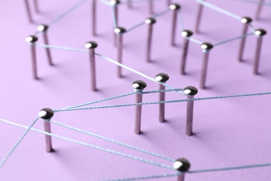 Photo of Network connection. Nails linked together by thread on violet background, closeup