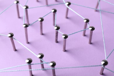 Photo of Network connection. Nails linked together by thread on violet background, closeup