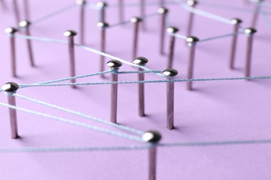 Photo of Network connection. Nails linked together by thread on violet background, closeup