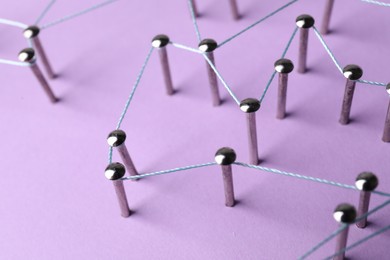 Photo of Network connection. Nails linked together by thread on violet background, closeup