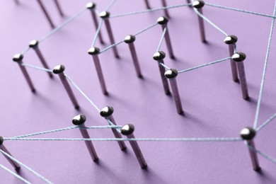 Photo of Network connection. Nails linked together by thread on violet background, closeup