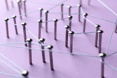 Photo of Network connection. Nails linked together by thread on violet background, closeup