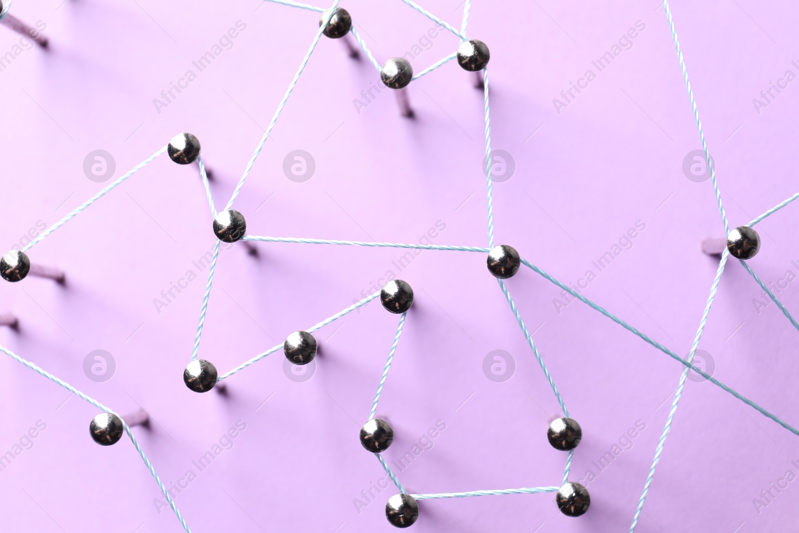 Photo of Network connection. Nails linked together by thread on violet background, flat lay