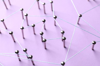 Photo of Network connection. Nails linked together by thread on violet background, closeup