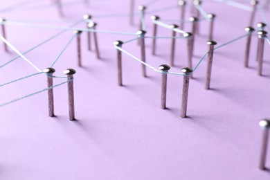 Photo of Network connection. Nails linked together by thread on violet background, closeup