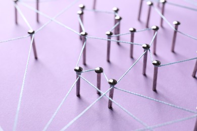 Photo of Network connection. Nails linked together by thread on violet background, closeup