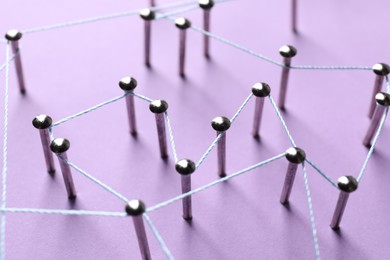 Photo of Network connection. Nails linked together by thread on violet background, closeup