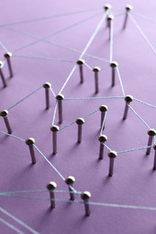 Photo of Network connection. Nails linked together by thread on violet background, closeup