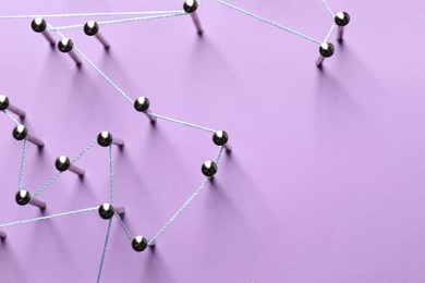 Photo of Network connection. Nails linked together by thread on violet background, flat lay. Space for text