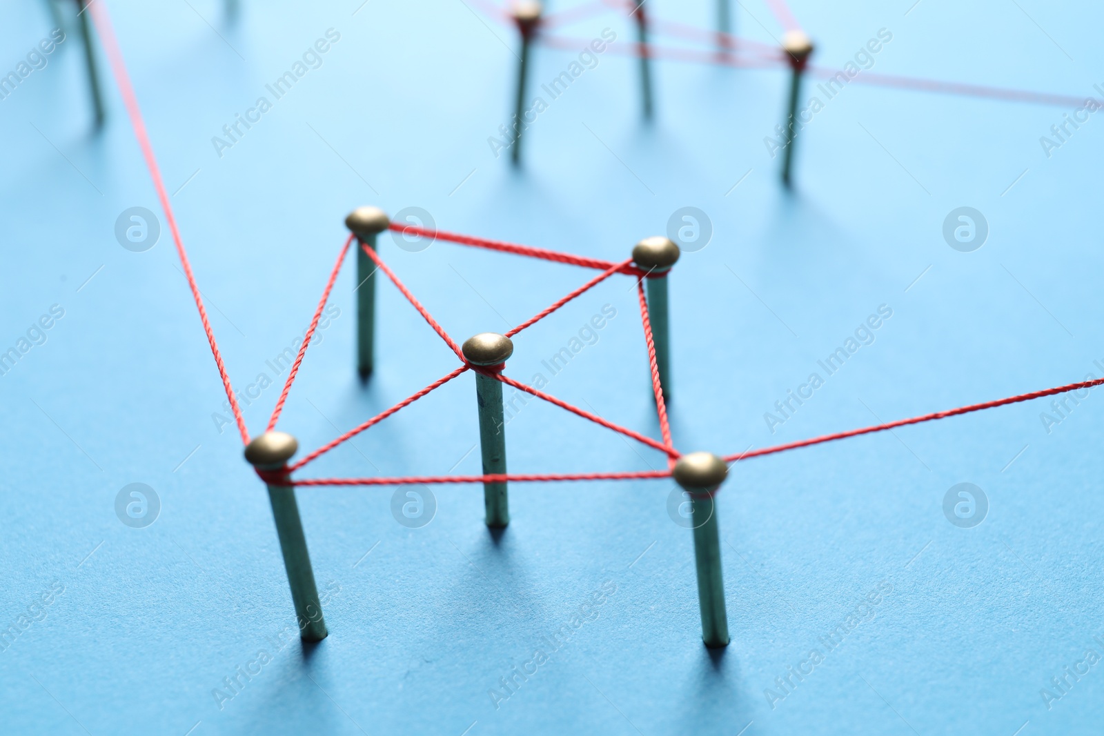 Photo of Network connection. Nails linked together by thread on light blue background, closeup