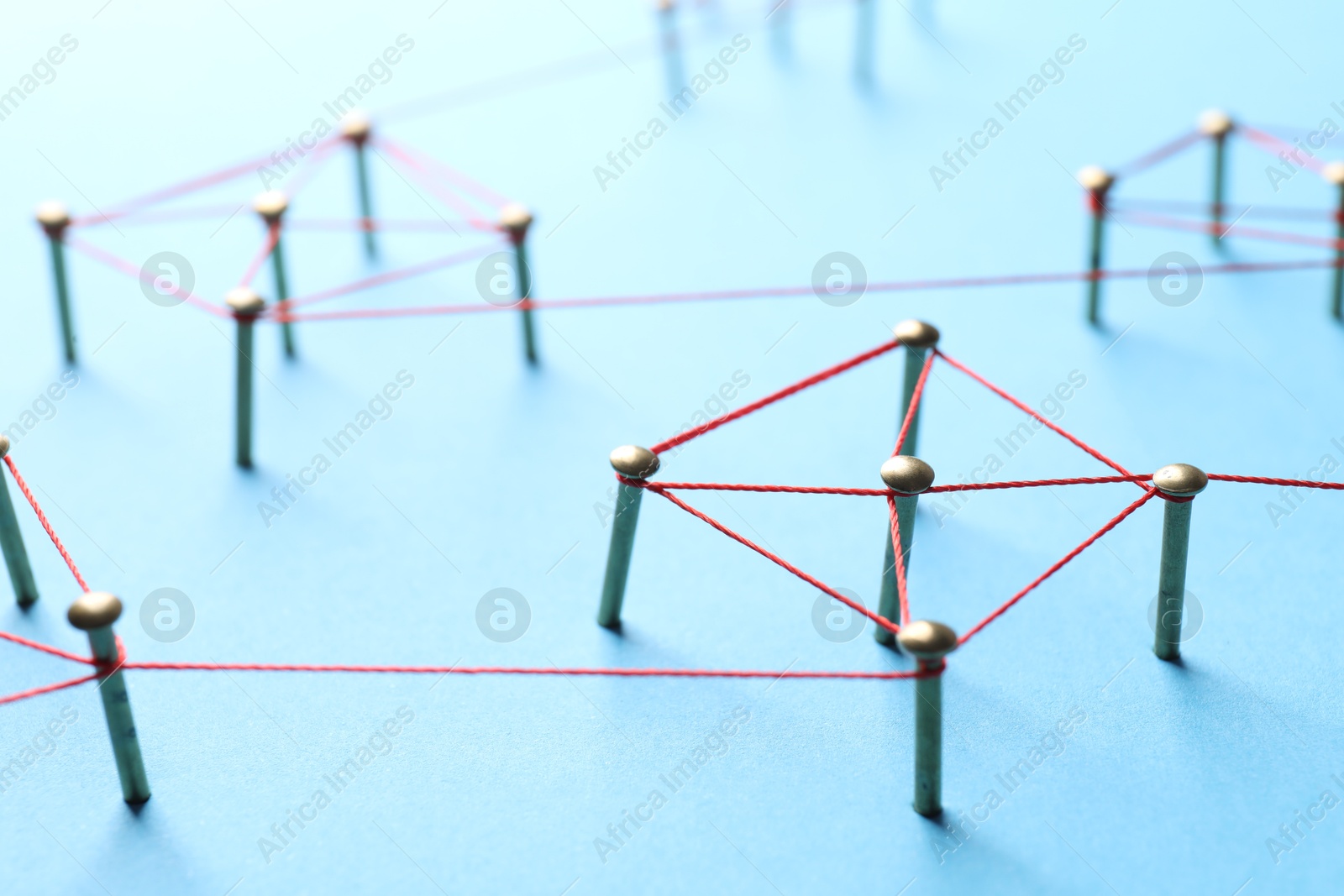 Photo of Network connection. Nails linked together by thread on light blue background, closeup