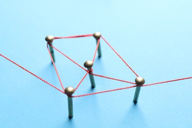 Photo of Network connection. Nails linked together by thread on light blue background, closeup