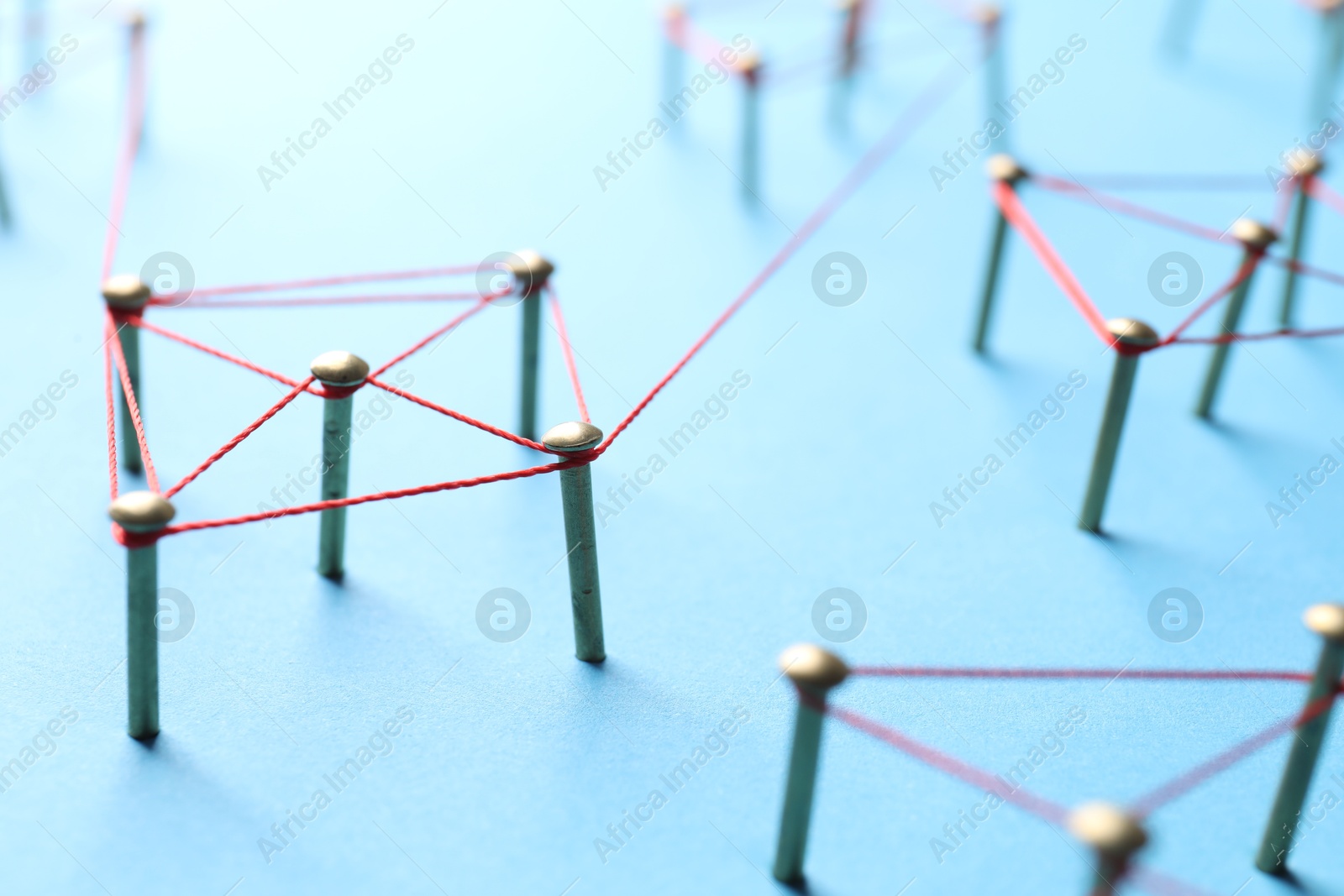 Photo of Network connection. Nails linked together by thread on light blue background, closeup