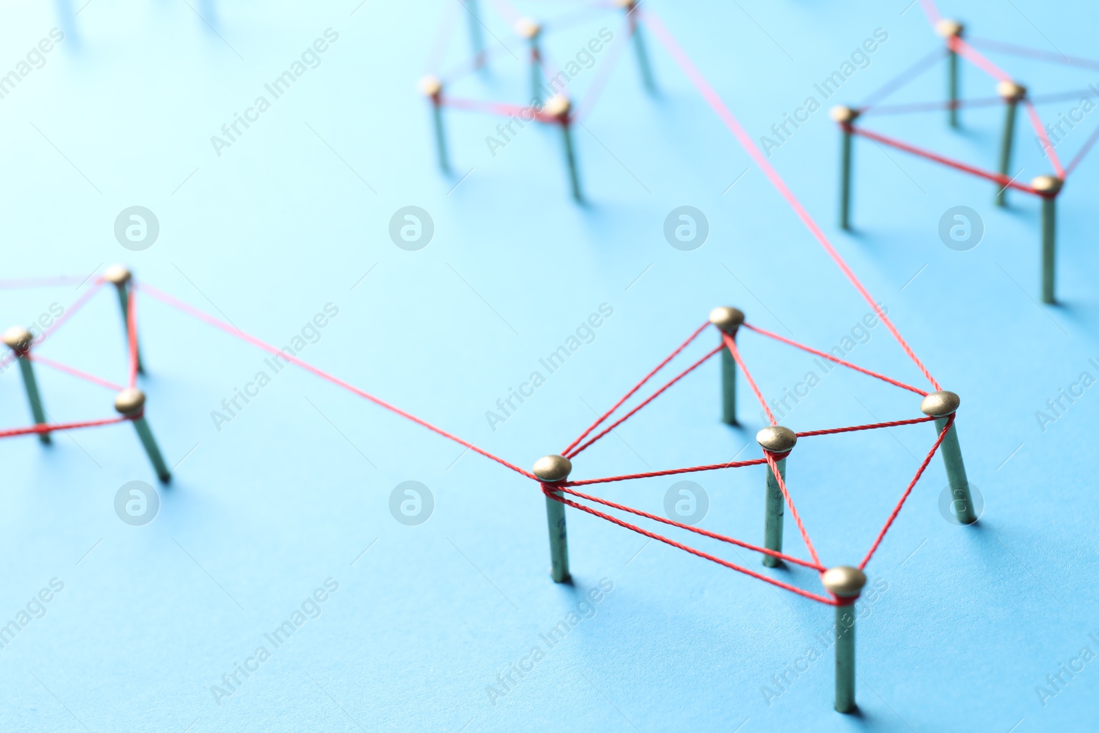 Photo of Network connection. Nails linked together by thread on light blue background, closeup