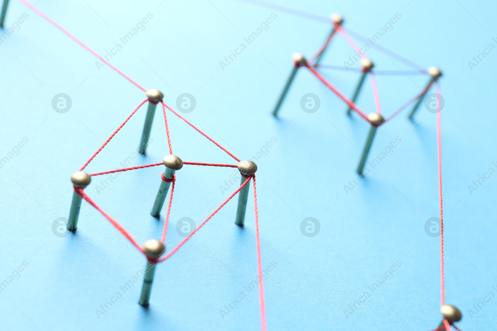 Photo of Network connection. Nails linked together by thread on light blue background, closeup