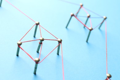 Photo of Network connection. Nails linked together by thread on light blue background, closeup