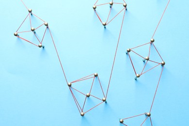 Photo of Network connection. Nails linked together by thread on light blue background, flat lay