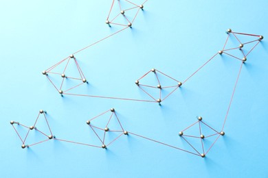 Photo of Network connection. Nails linked together by thread on light blue background, flat lay