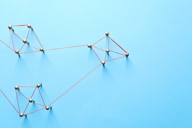 Photo of Network connection. Nails linked together by thread on light blue background, flat lay. Space for text