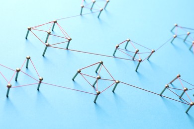 Photo of Network connection. Nails linked together by thread on light blue background, closeup