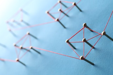 Photo of Network connection. Nails linked together by thread on light blue background, closeup