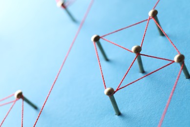 Photo of Network connection. Nails linked together by thread on light blue background, closeup