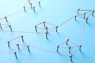 Photo of Network connection. Nails linked together by thread on light blue background, closeup