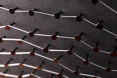 Photo of Network connection. Nails linked together by thread on black background, above view