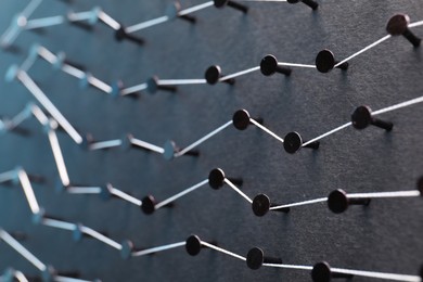 Photo of Network connection. Nails linked together by thread on black background, closeup