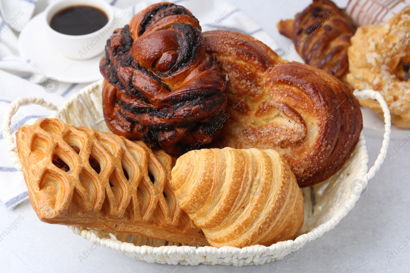 Photo of Different pastries in basket and coffee on light table, closeup