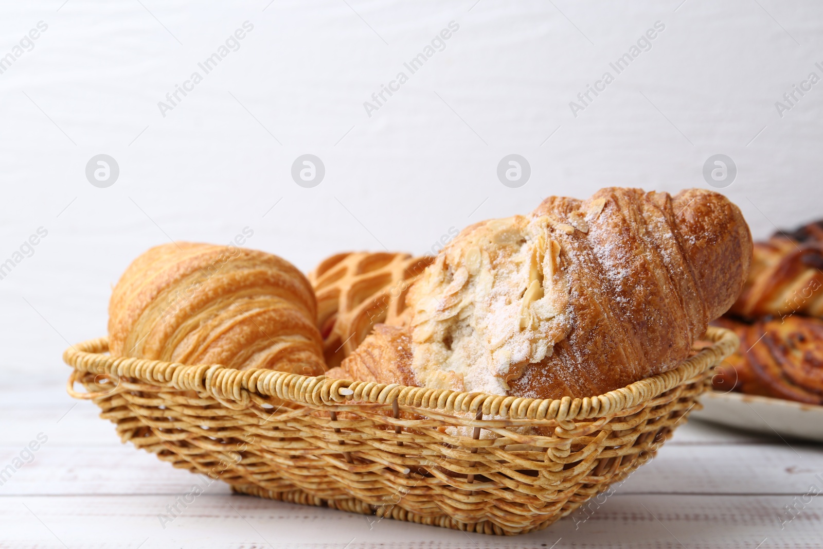 Photo of Different pastries in basket on white wooden table