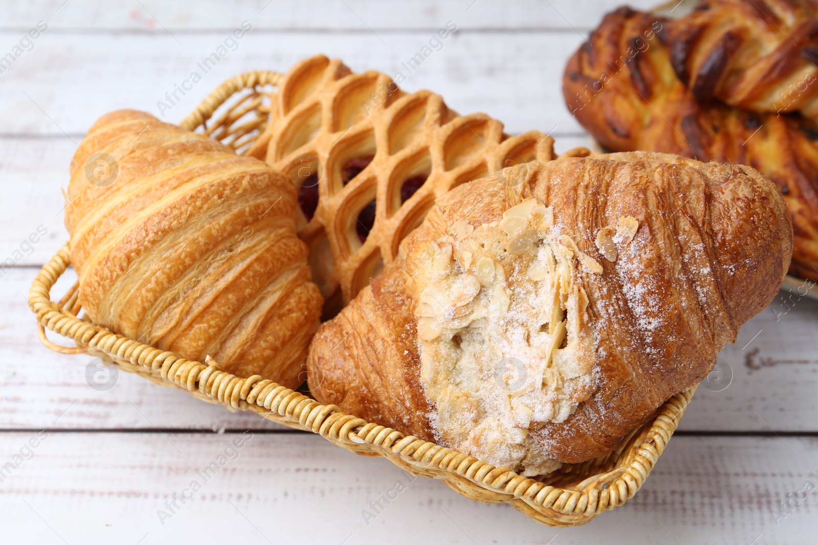 Photo of Different pastries in basket on white wooden table, closeup