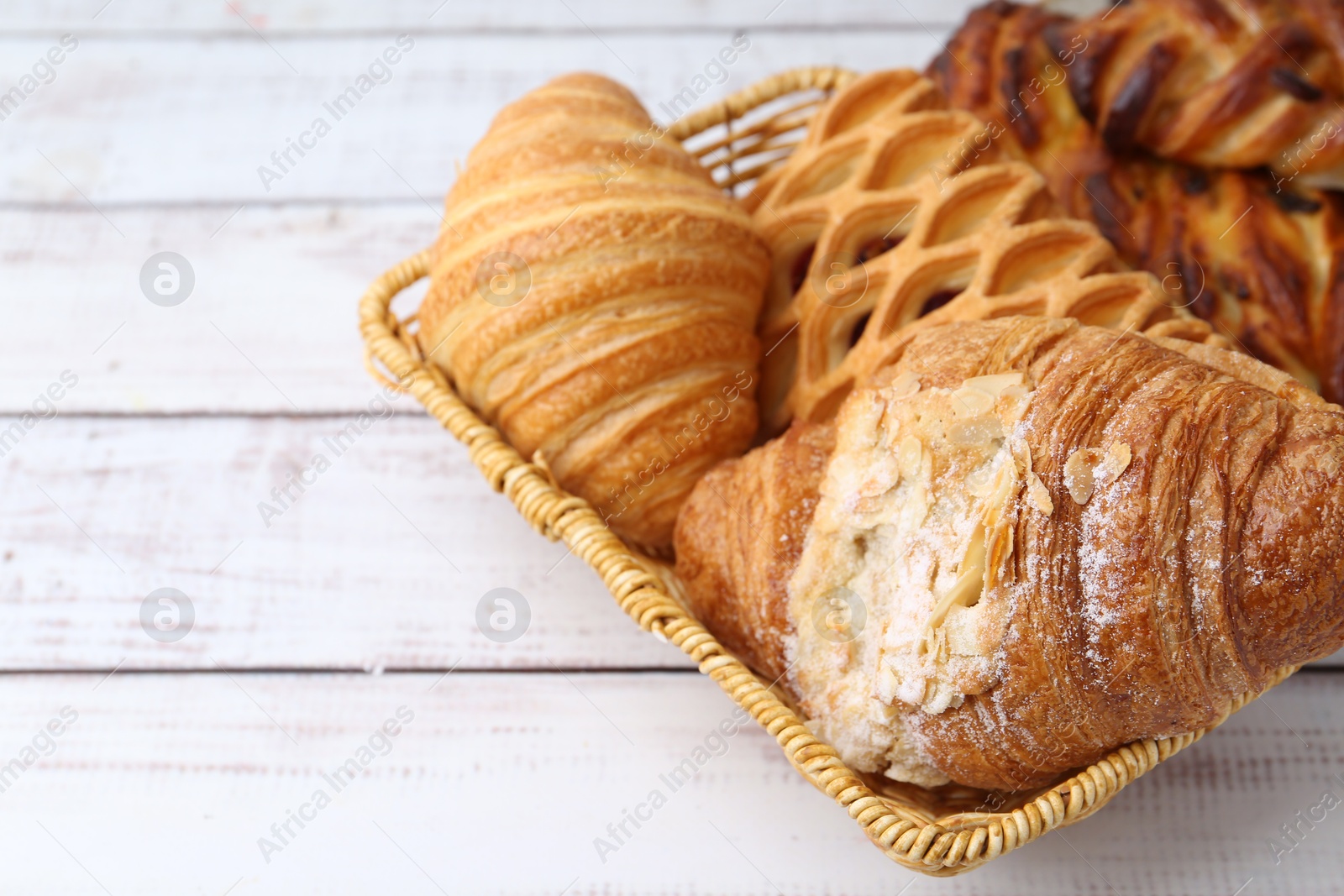 Photo of Different pastries in basket on white wooden table, closeup. Space for text