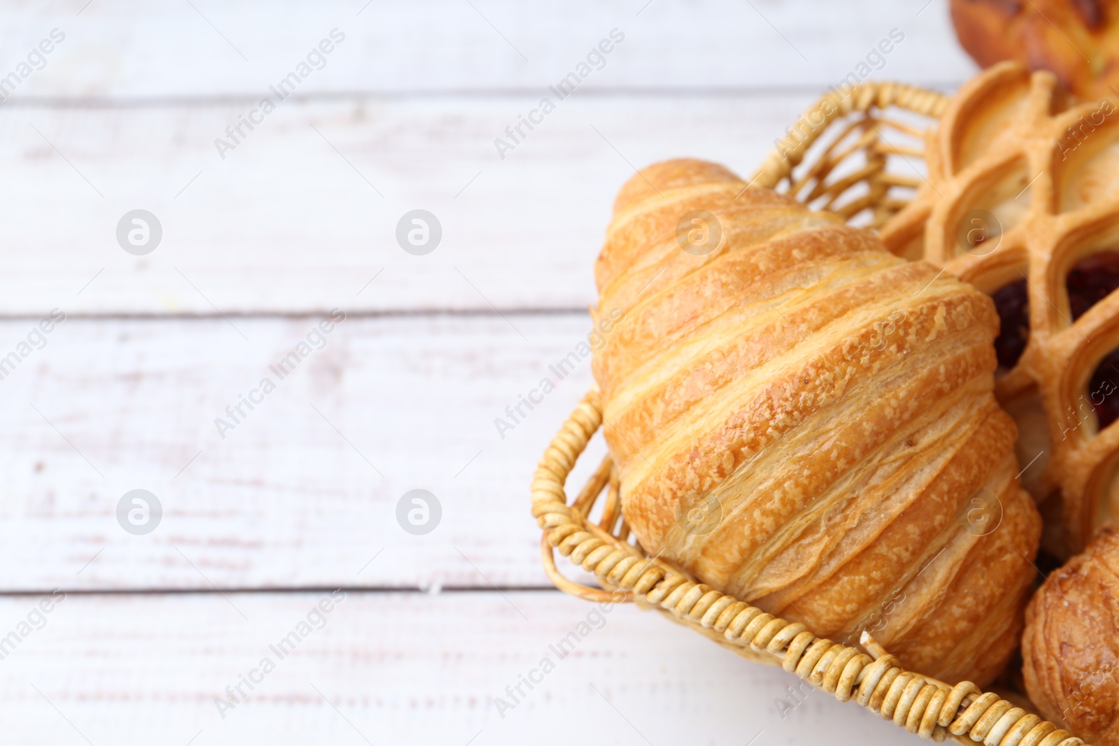 Photo of Different pastries in basket on white wooden table, closeup. Space for text