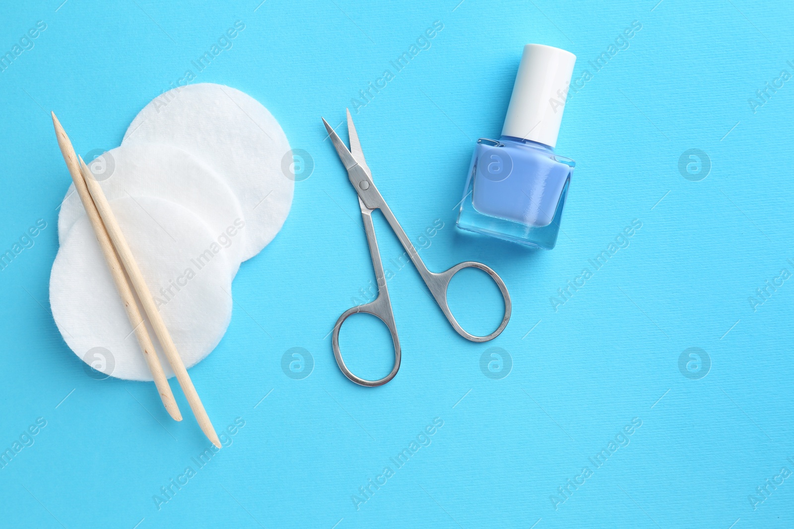 Photo of Pedicure procedure. Nail polish, scissors, orange sticks and cotton pads on light blue background, flat lay