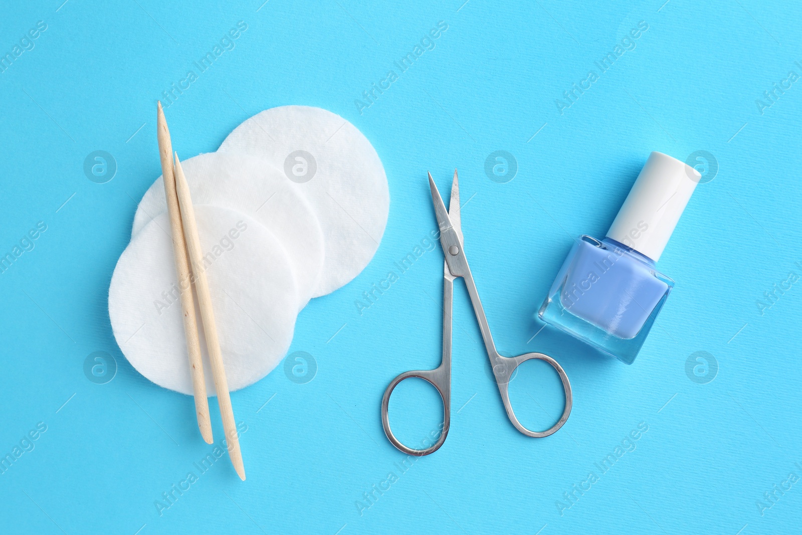 Photo of Pedicure procedure. Nail polish, scissors, orange sticks and cotton pads on light blue background, flat lay