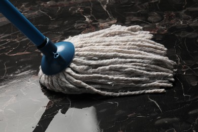 Photo of Cleaning black marble floor with string mop, closeup