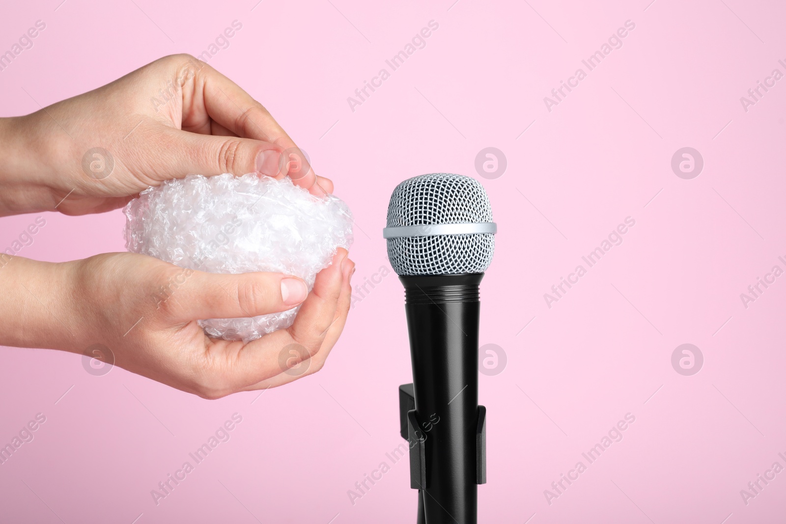 Photo of Woman making ASMR sounds with microphone and bubble wrap on pink background, closeup