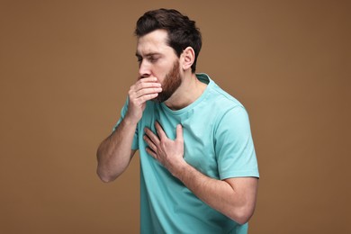 Photo of Sick man coughing on brown background. Cold symptoms