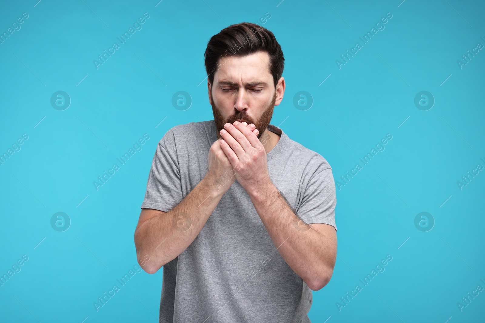 Photo of Sick man coughing on light blue background. Cold symptoms