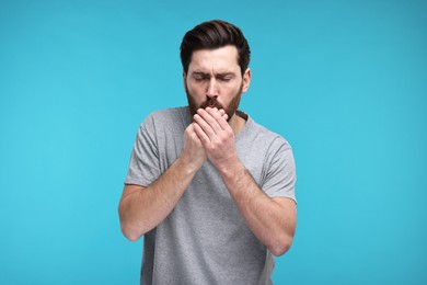 Photo of Sick man coughing on light blue background. Cold symptoms